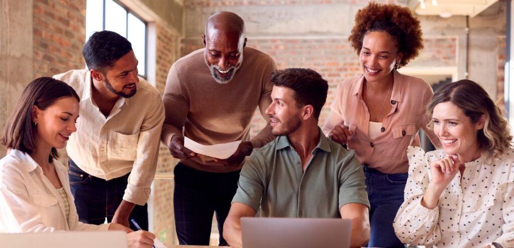 A diverse team of SaaS sales professionals collaborating in an open office environment. They are engaged in a lively discussion, with charts and graphs on a whiteboard in the background, illustrating the dynamic and interactive nature of SaaS sales roles.