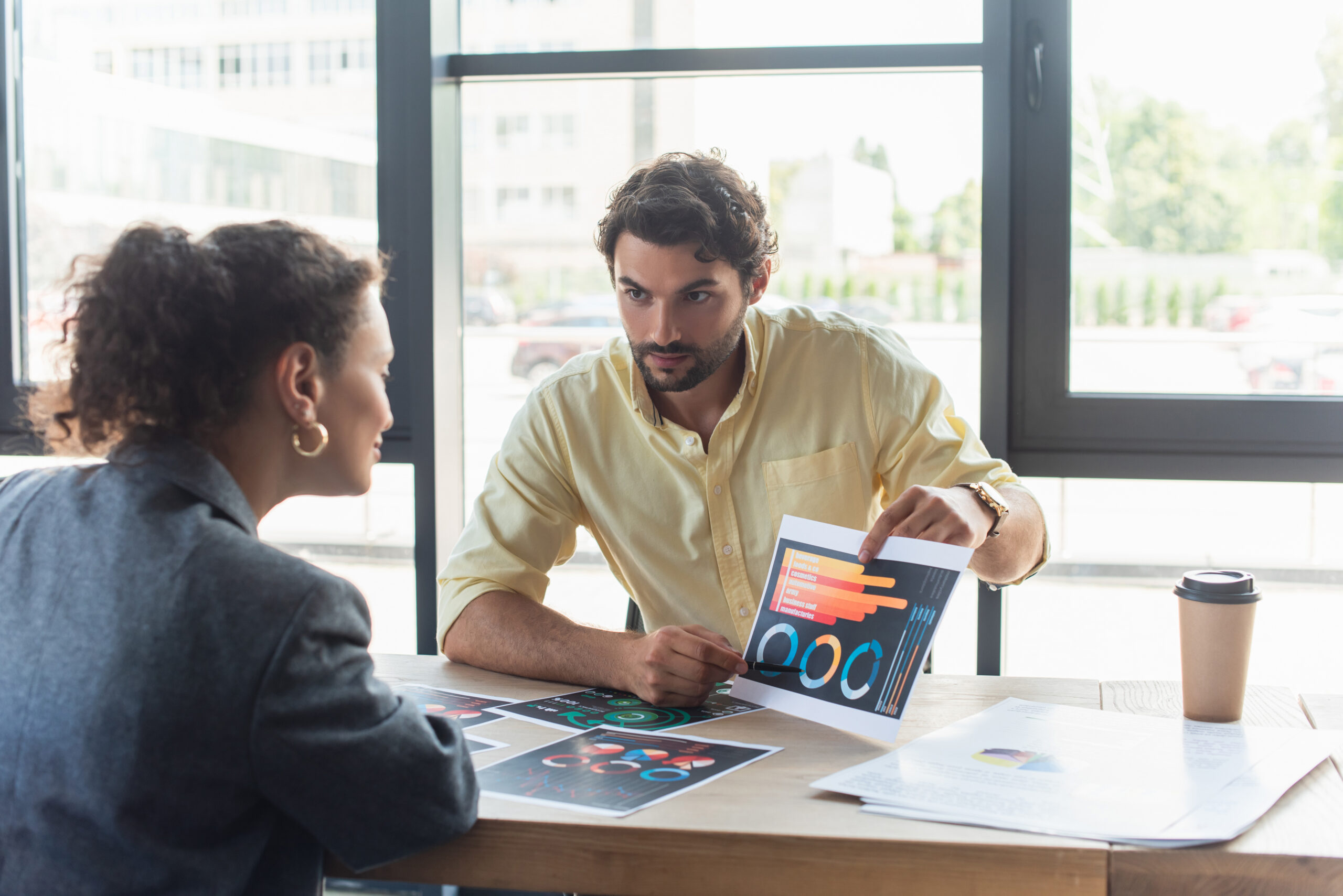 SaaS Sales Businessman pointing at charts on SaaS document near african american colleague in office